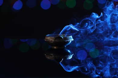 Blown out diya on dark background with blurred lights, space for text. Diwali lamp