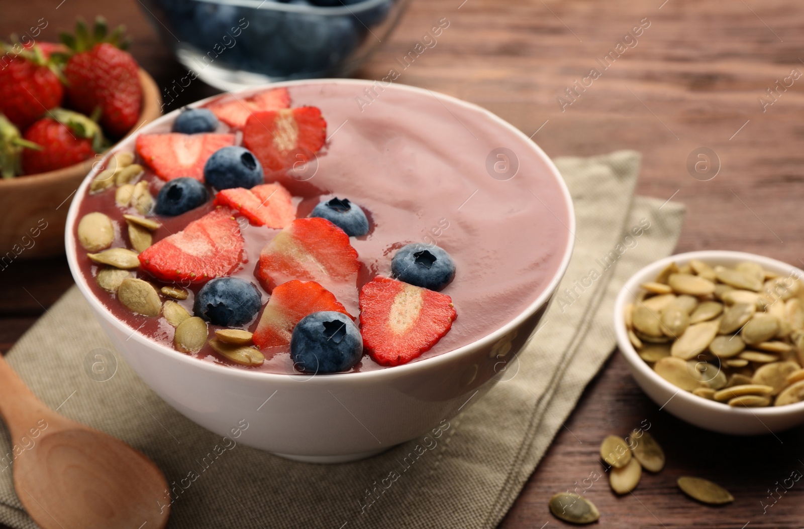 Photo of Bowl of delicious smoothie with fresh blueberries, strawberries and pumpkin seeds on wooden table