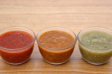 Photo of Different tasty salsa sauces on wooden table, closeup