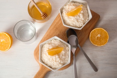 Photo of Creamy rice pudding with orange slices in bowls served on wooden table, top view
