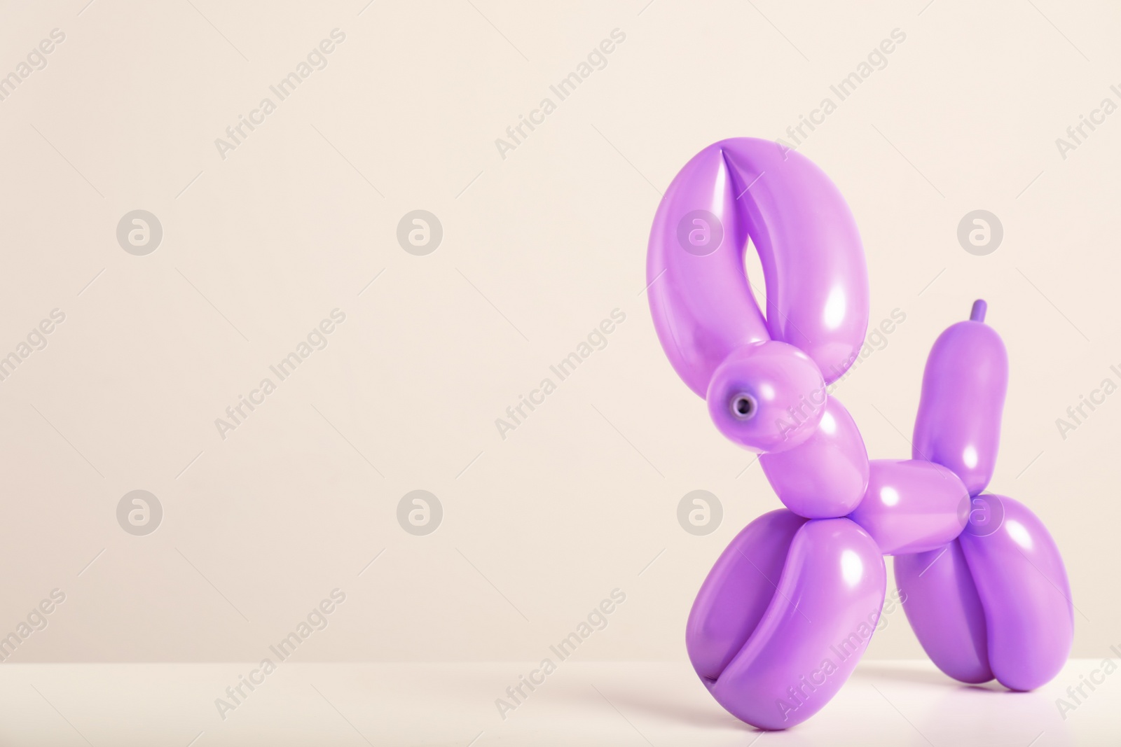 Photo of Animal figure made of modelling balloon on table against color background. Space for text