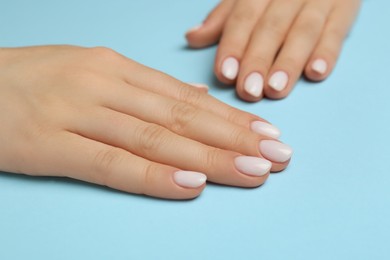 Woman showing her manicured hands with white nail polish on light blue background, closeup