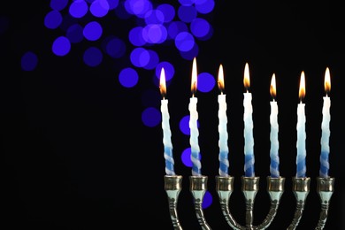 Photo of Hanukkah celebration. Menorah with burning candles against dark background with blurred lights, space for text