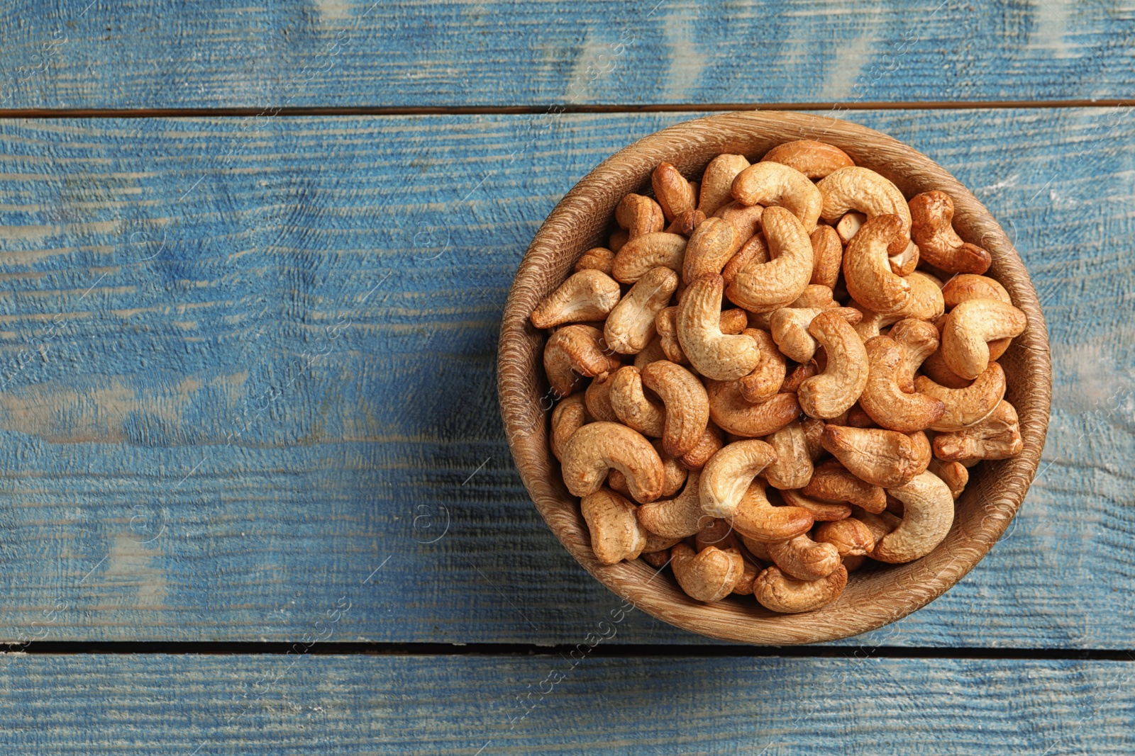 Photo of Tasty cashew nuts in bowl on color wooden table, top view. Space for text