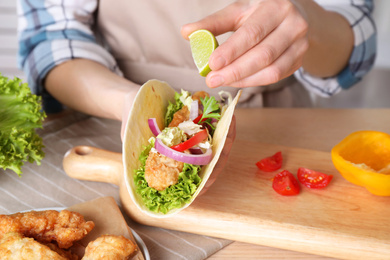 Photo of Woman squeezing lime on fish taco at table, closeup