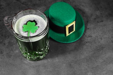 Photo of St. Patrick's day celebration. Green beer with decorative clover leaf and leprechaun hat on grey table. Space for text