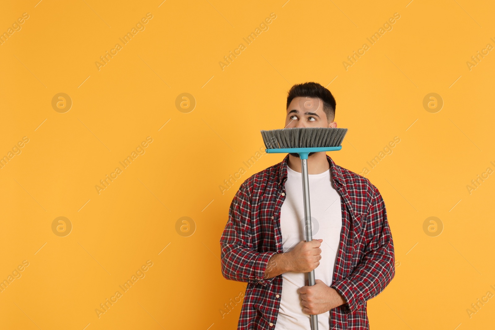 Photo of Young man with broom on orange background, space for text