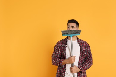 Young man with broom on orange background, space for text