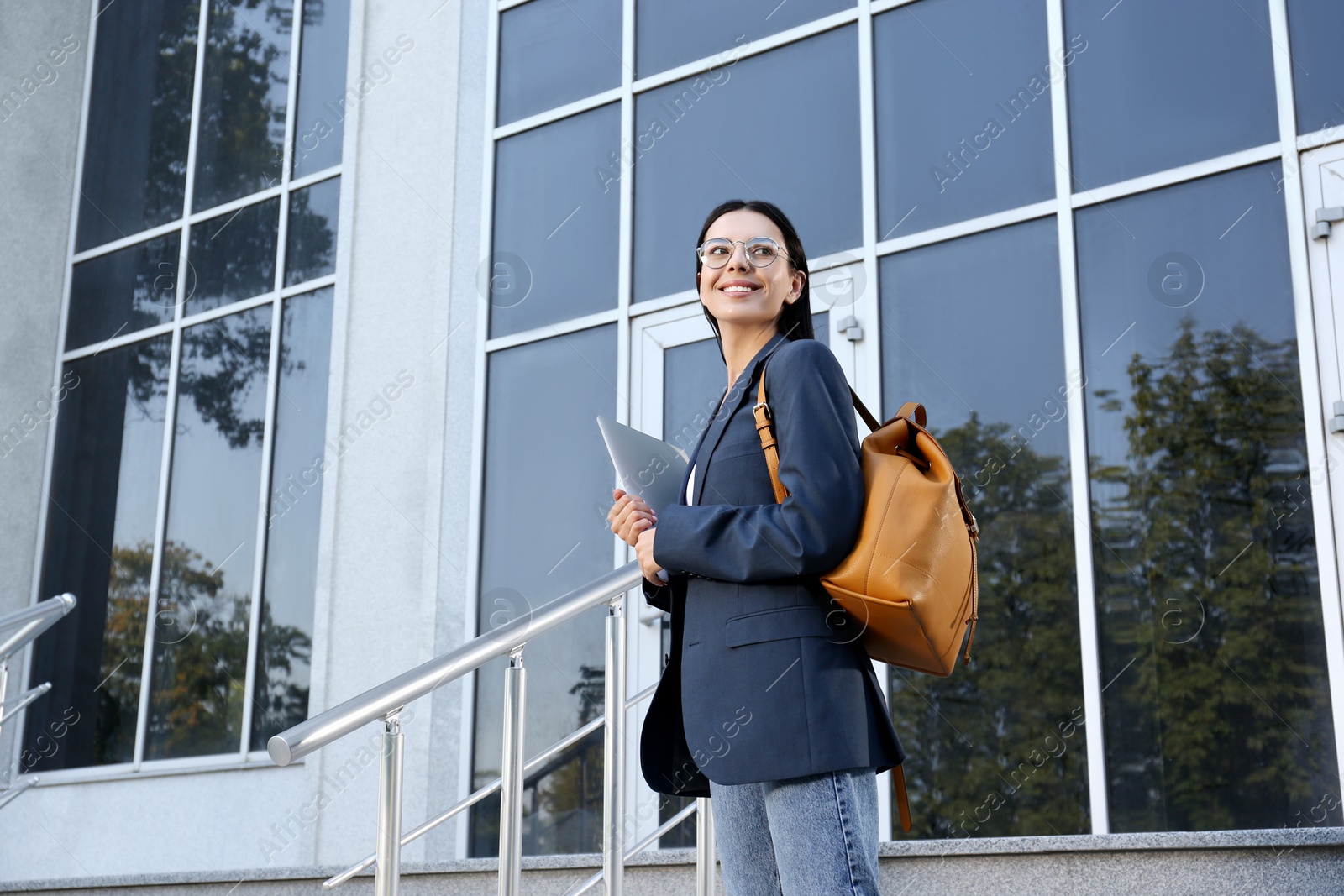 Photo of Beautiful young woman with stylish backpack and laptop near building outdoors