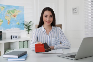 Happy manager holding passports at desk in travel agency
