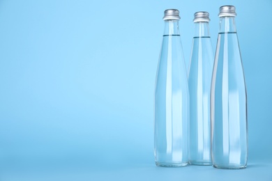Glass bottles with water on light blue background, space for text