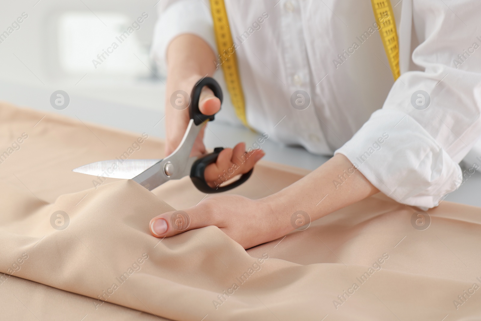 Photo of Dressmaker cutting fabric with scissors at table in atelier, closeup