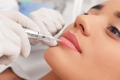 Young woman undergoing procedure of permanent lip makeup in tattoo salon, closeup