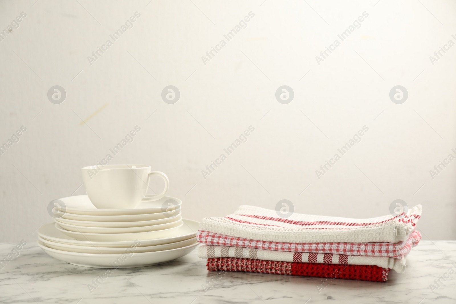 Photo of Stacked kitchen towels and dishware on white marble table, space for text