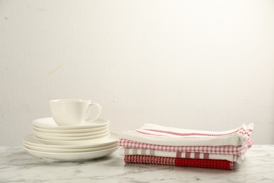 Photo of Stacked kitchen towels and dishware on white marble table, space for text