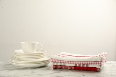 Stacked kitchen towels and dishware on white marble table, space for text