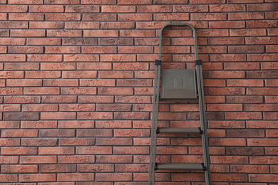 Metal stepladder near brick wall. Space for text