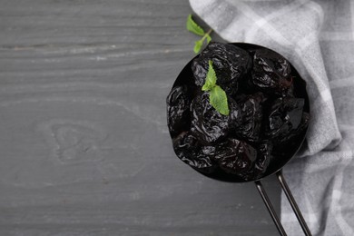 Photo of Sweet dried prunes and mint in scoop on grey wooden table, top view. Space for text