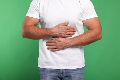 Photo of Man suffering from stomach pain on green background, closeup