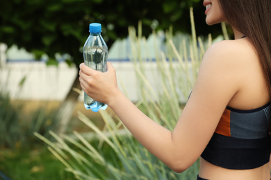 Photo of Sportswoman with bottle of water outdoors, closeup