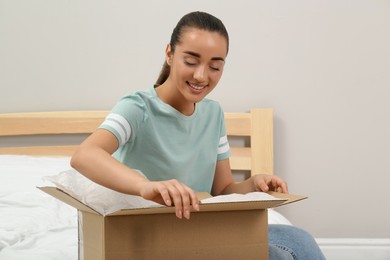 Happy young woman opening parcel on bed at home. Internet shopping