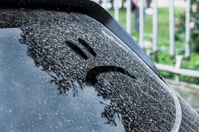 Sad emoticon drawn on dirty car window outdoors, closeup