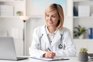 Photo of Smiling doctor with laptop having online consultation at table in office