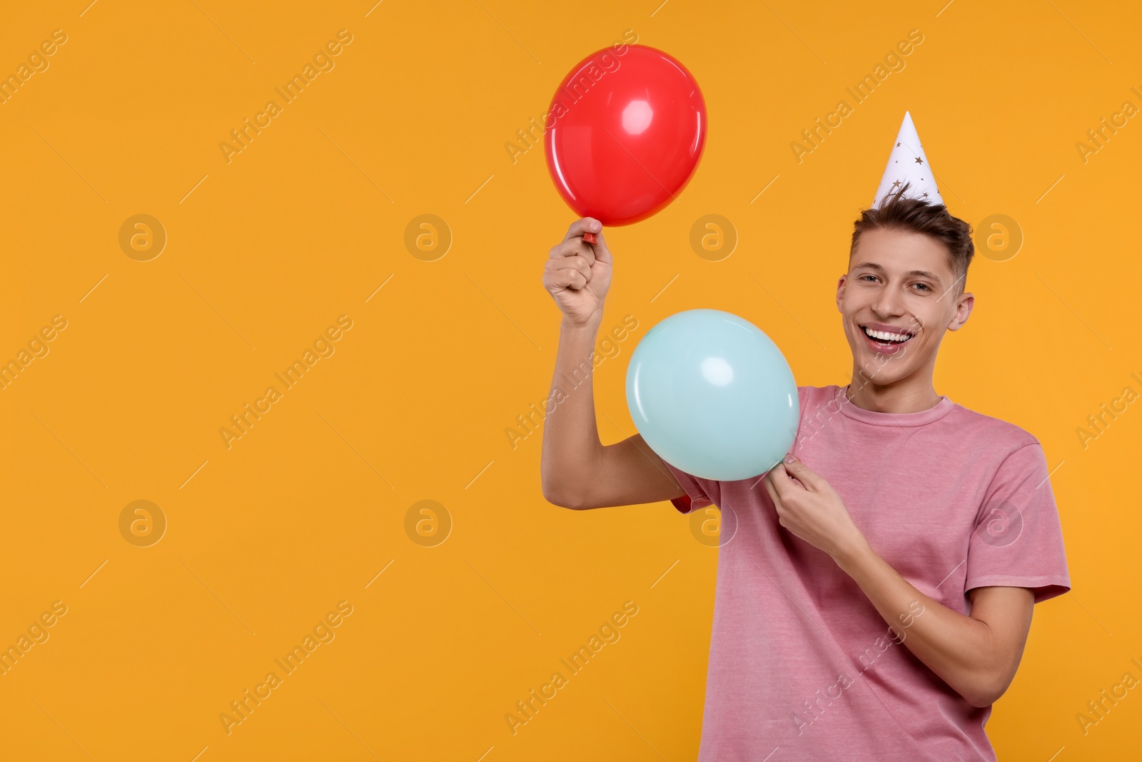 Photo of Happy man in party hat with balloons on orange background. Space for text