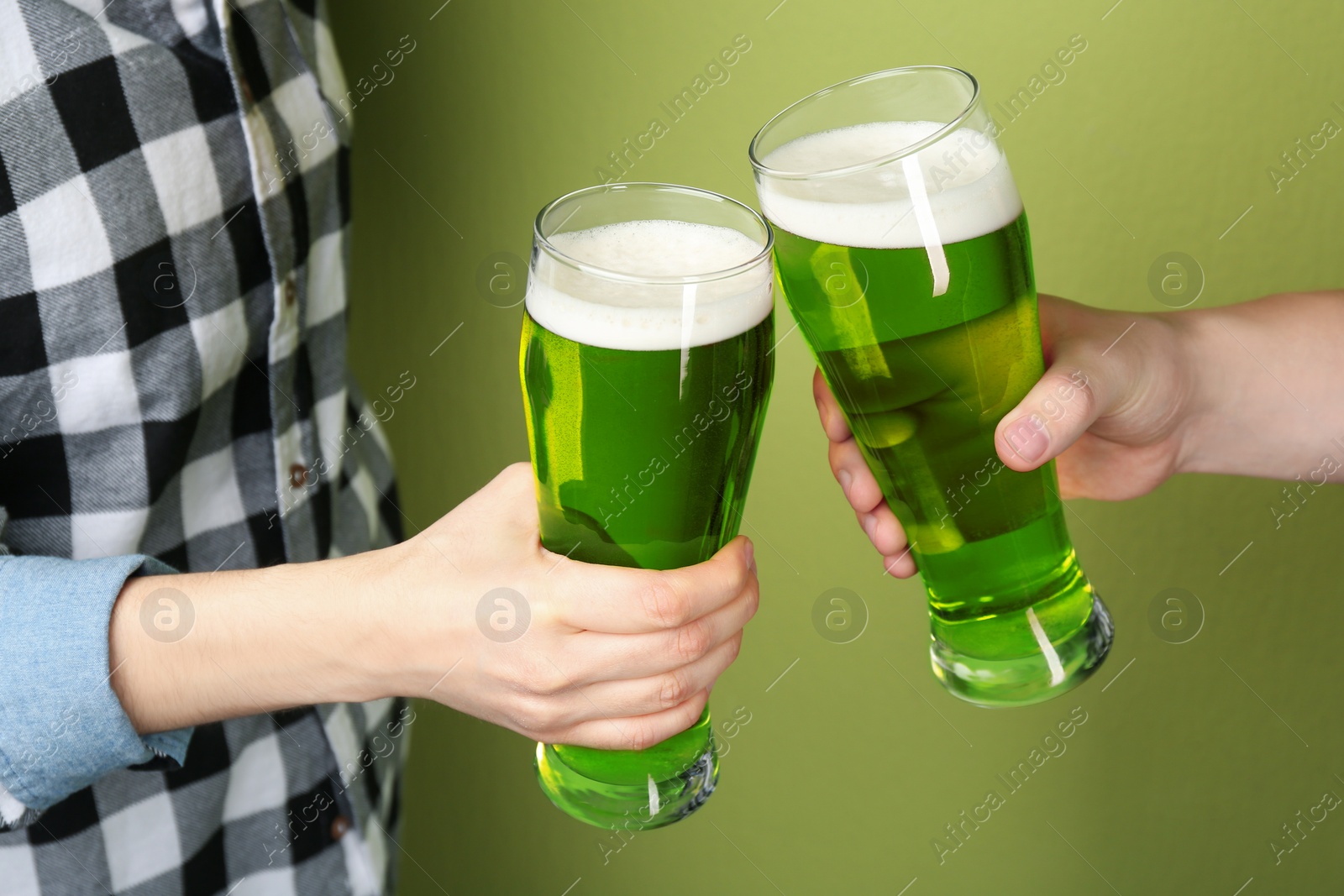 Photo of Man and woman toasting with green beer on color background, closeup. St. Patrick's Day celebration