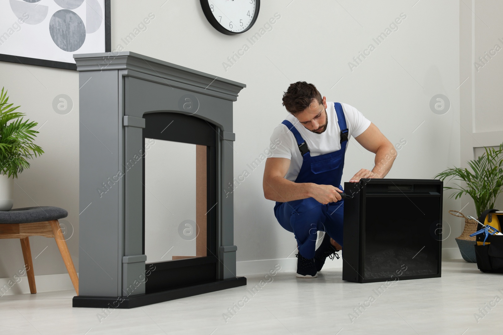 Photo of Professional technician with screwdriver installing electric fireplace in room