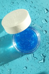 Photo of Open jar of cosmetic product on wet turquoise background, top view