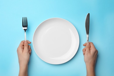 Photo of Woman with fork, knife and empty plate on color background, top view
