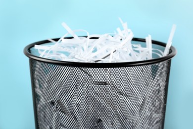 Trash bin with shredded paper strips on light blue background