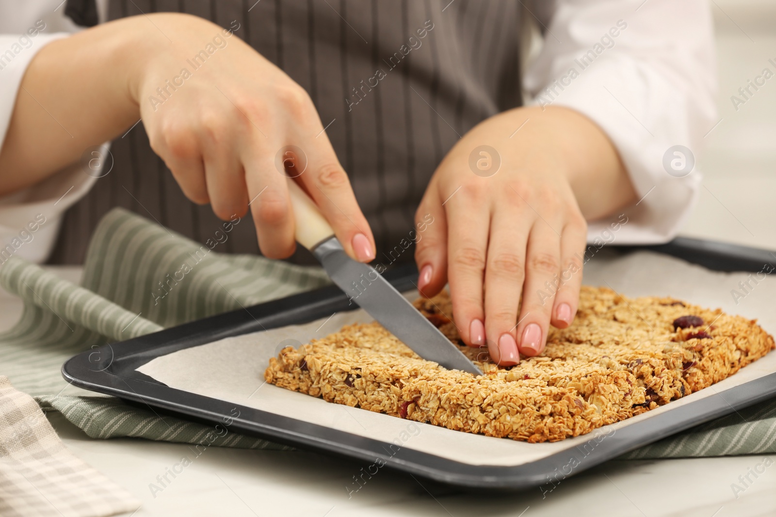 Photo of Woman cutting granola bars at table in kitchen, closeup