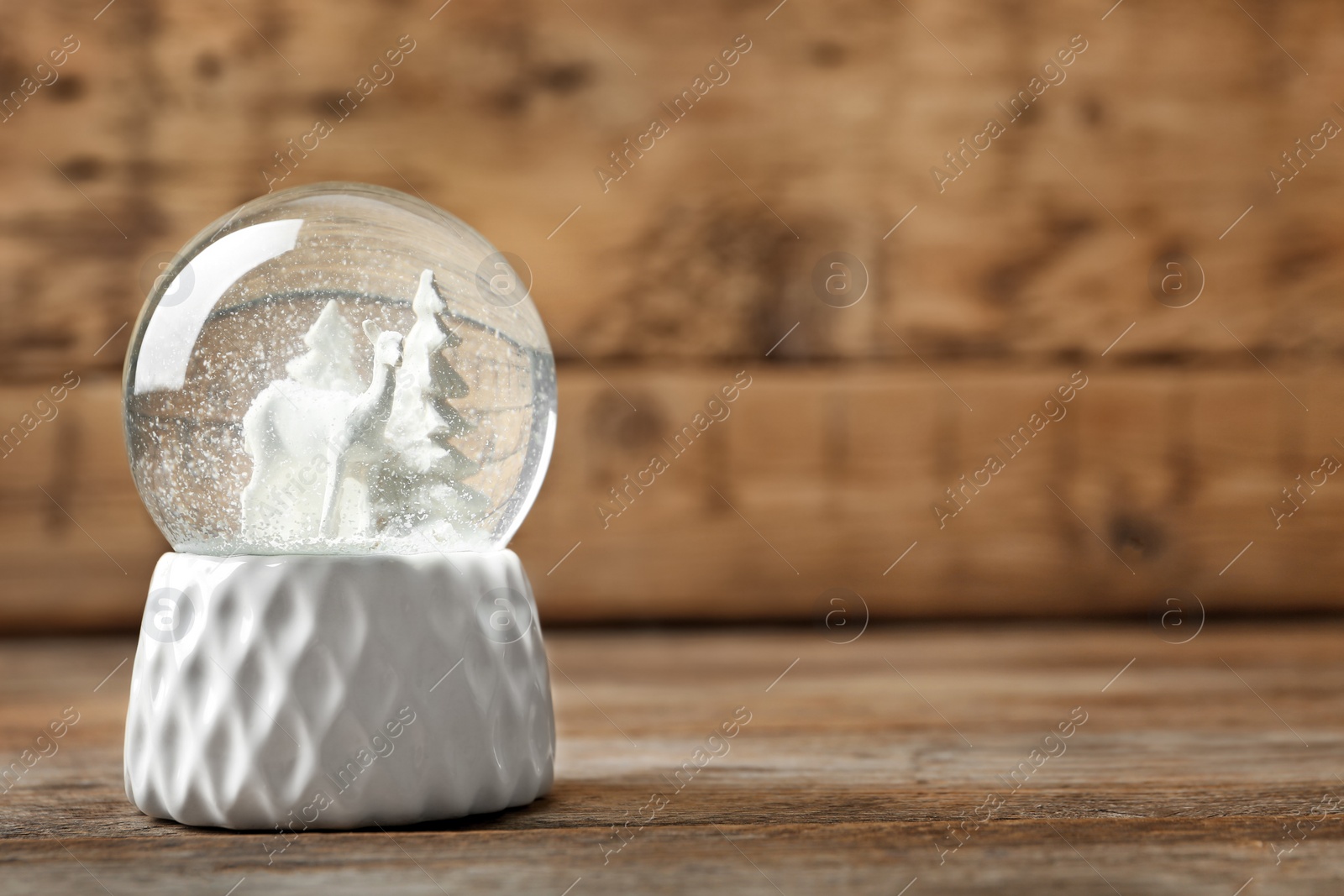 Photo of Snow globe with deer and trees on wooden table, space for text. Christmas season