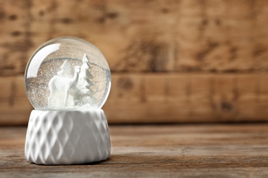 Snow globe with deer and trees on wooden table, space for text. Christmas season