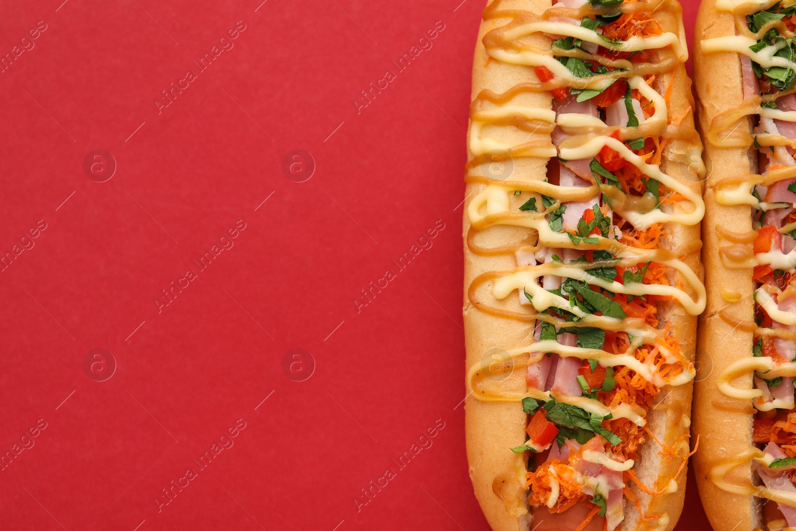 Photo of Delicious hot dogs with bacon, carrot and parsley on red background, top view. Space for text