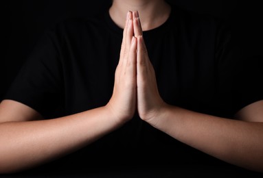 Photo of Woman holding hands clasped while praying against black background, closeup