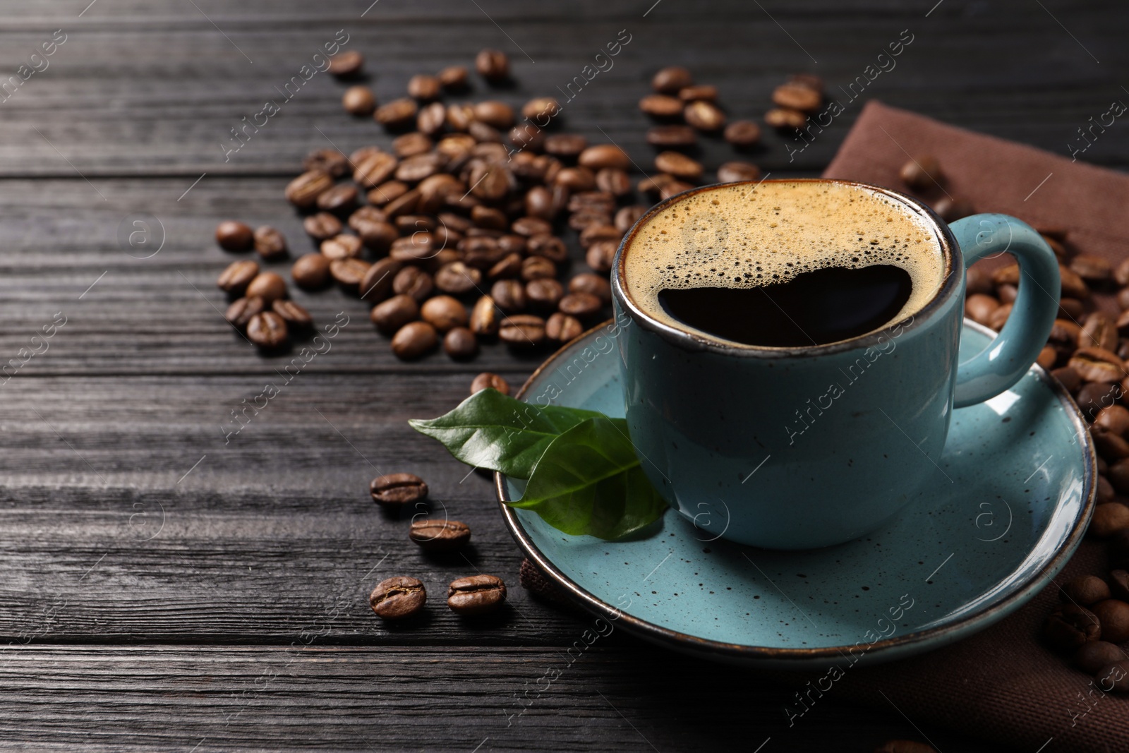 Photo of Cup of aromatic hot coffee and beans on black wooden table, space for text