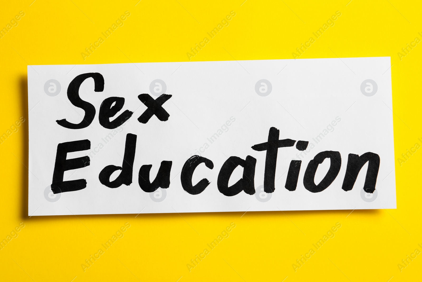 Photo of Piece of paper with phrase "SEX EDUCATION" on yellow background, top view