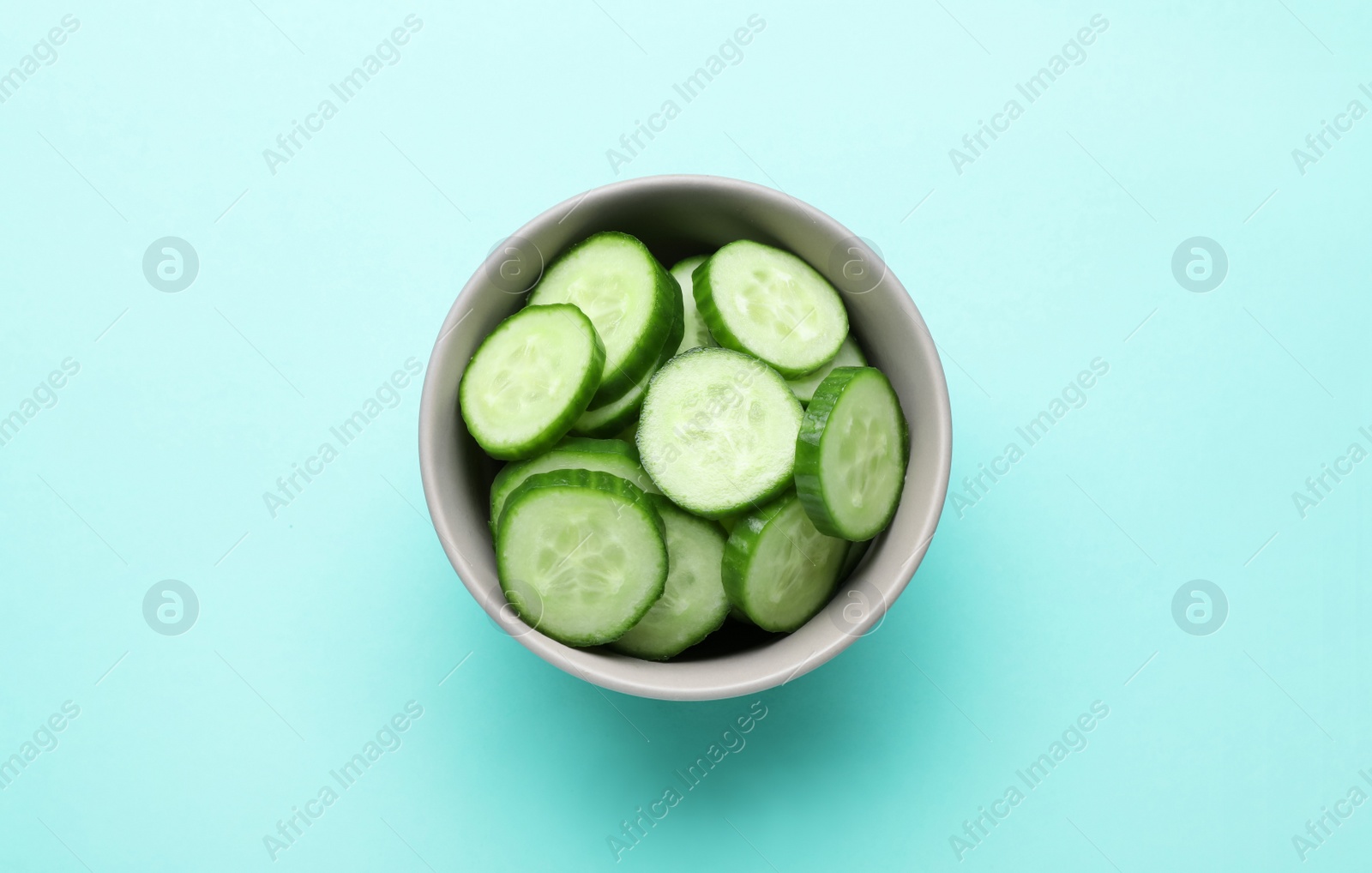 Photo of Slices of fresh ripe cucumber in bowl on light blue background, top view