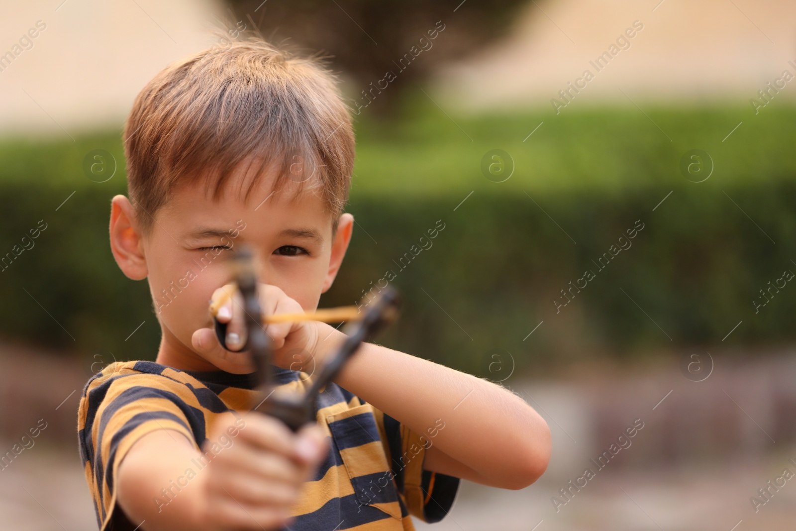 Photo of Little boy playing with slingshot outdoors. Space for text