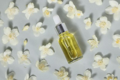 Photo of Essential oil in bottle and beautiful jasmine flowers on grey background, flat lay