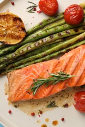 Photo of Tasty grilled salmon with tomatoes, asparagus and spices on plate, top view