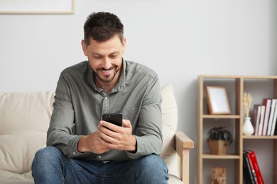 Photo of Happy handsome man using smartphone at home