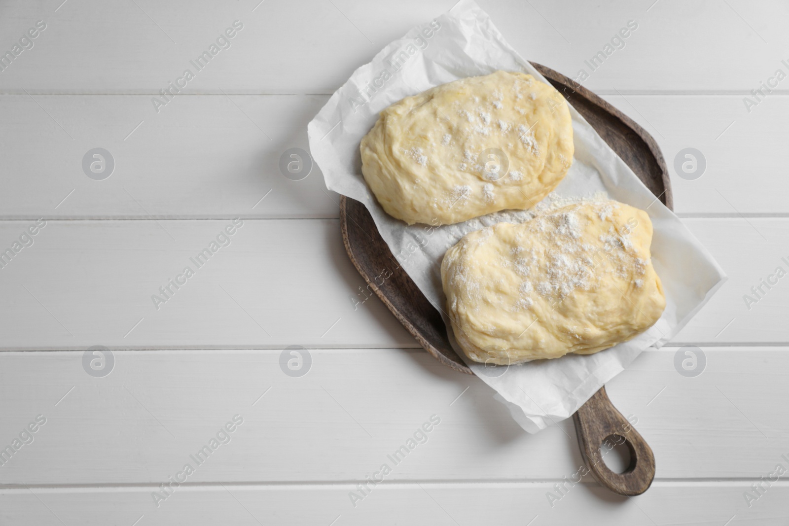 Photo of Raw dough and flour on white wooden table, top view with space for text. Cooking ciabatta