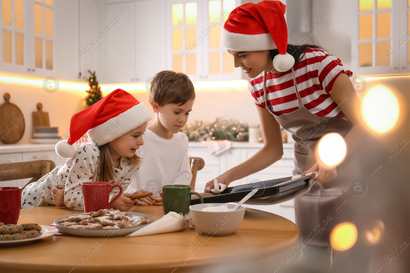 Photo of Mother giving her cute little children freshly baked Christmas cookies in kitchen