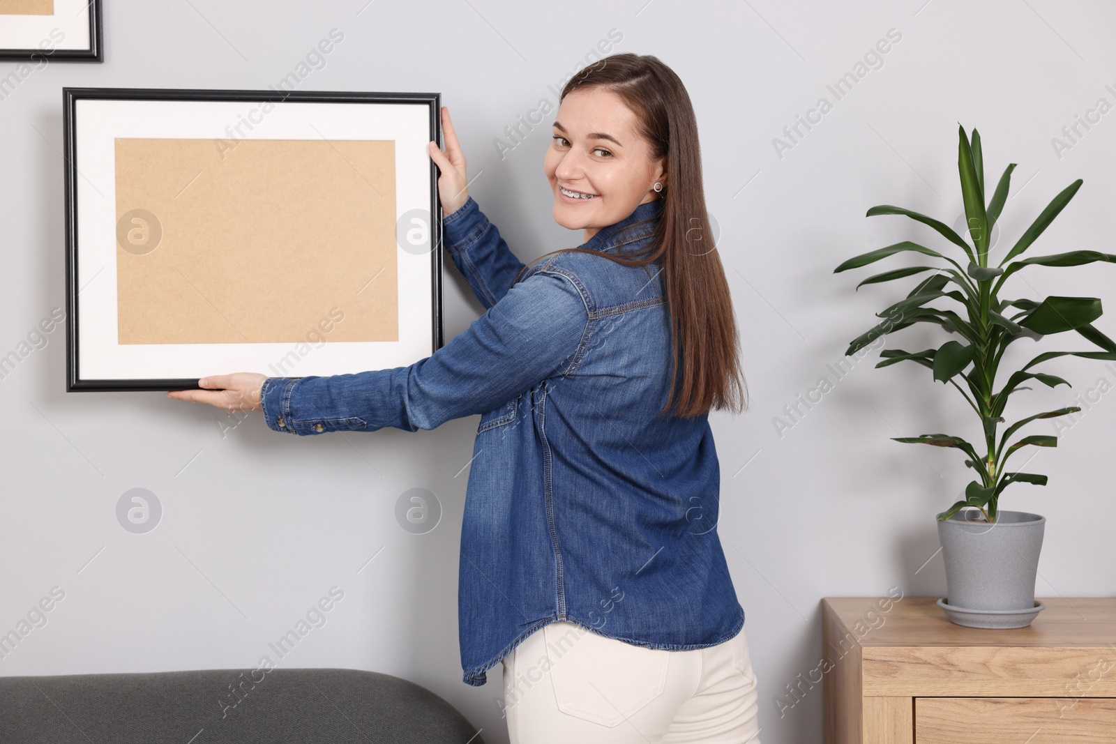 Photo of Woman hanging picture frame on gray wall at home