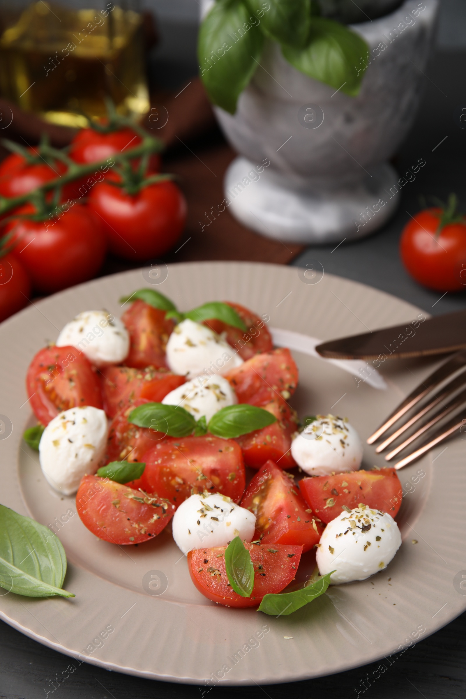 Photo of Tasty salad Caprese with mozarella balls, tomatoes and basil served on grey table