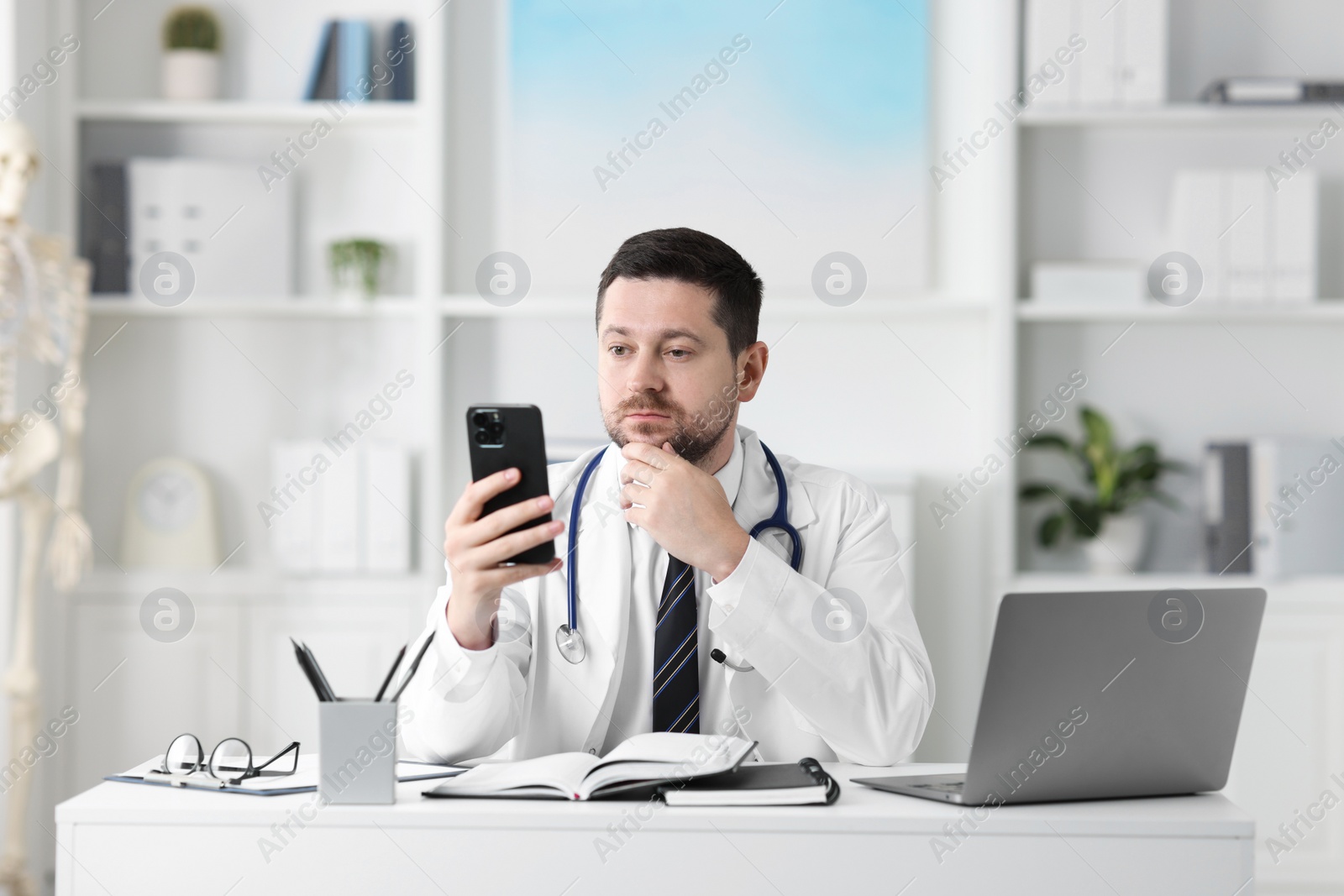 Photo of Doctor having online consultation via smartphone at table in clinic